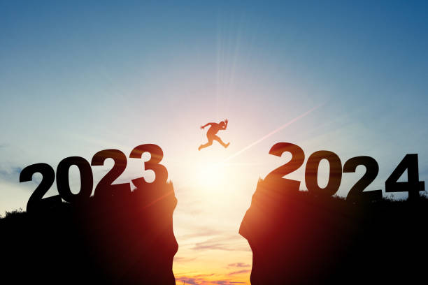 Welcome merry Christmas and happy new year in 2024,Silhouette Man jumping from 2023cliff to 2024 cliff with cloud sky and sunlight.