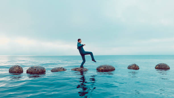 Man walks carefully on a path of small rocks in the middle of the sea. He looks focused and moves in the right direction. Concept of success and avoiding problems on the way of a journey or career path. 
Note: The man is a 3D-render with face scan. Model release attached.