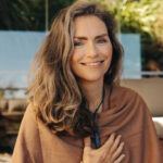 Senior woman smiling at the camera while wearing a crystal necklace. Mature woman meditating and practicing crystal healing at home. Happy senior woman following a holistic lifestyle.