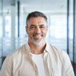 Headshot close up portrait of indian or latin confident mature good looking middle age leader, ceo male businessman on blur office background. Handsome hispanic senior business man smiling at camera.