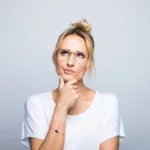 Thoughtful blond woman with hand on chin looking up against gray background